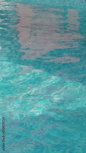 Blue water in a swimming pool with building reflections and visible mosaic tiles at the bottom. Gentle ripples create a dynamic play of light and color

