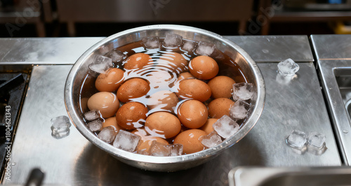 A stainless steel bowl of bolied eggs in a cold water and ice