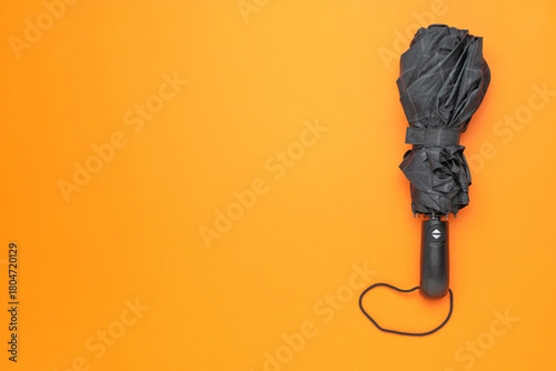 Closed Black Umbrella on Vibrant Orange Background - Minimalist Stock Photo for Weather and Fashion Concepts