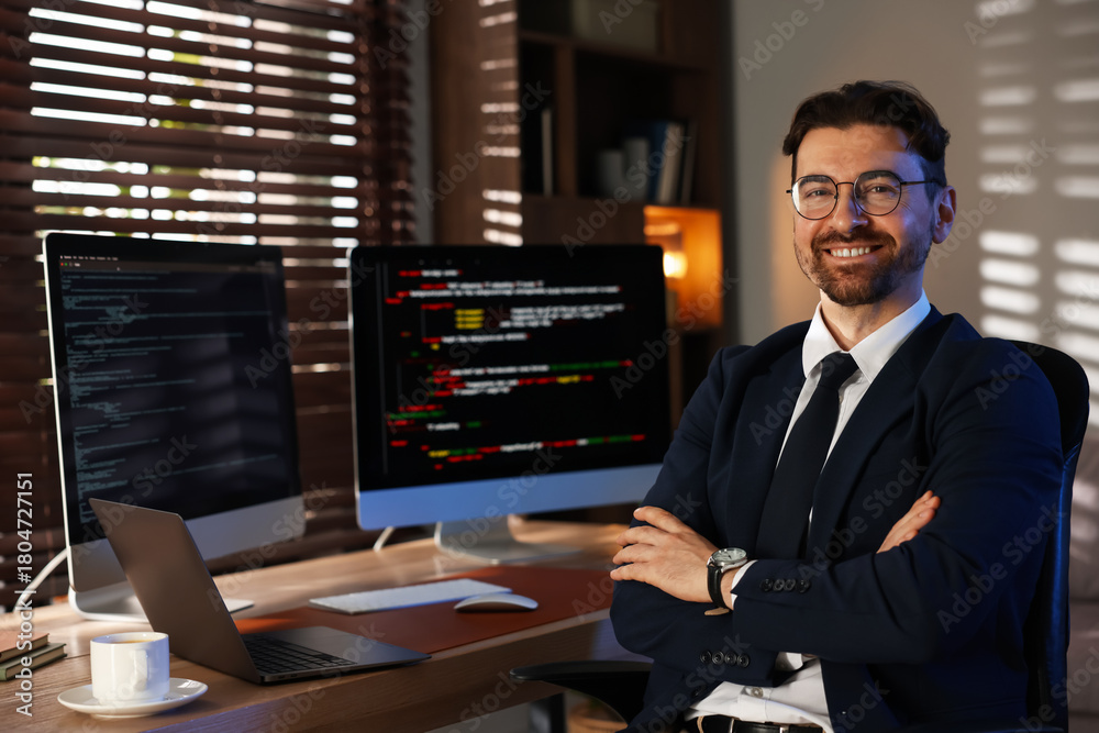 Fototapeta premium Portrait of smiling programmer in glasses and suit with crossed arms on chair at workplace