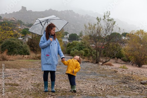 Real Mother and Daughter in Rainy Weather with Raincoats and Umbrella.