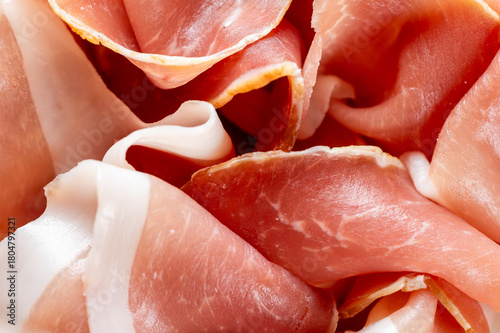 A close-up, macro photo of thinly sliced, delicate Italian prosciutto crudo or Spanish Jamón Serrano with red meat and white fat marbling and texture