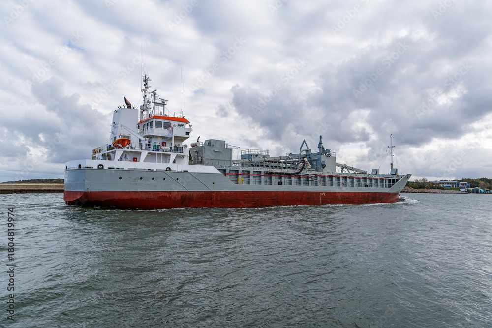 Fototapeta premium Cargo Ship Maneuvering Near Shoreline on Overcast Day