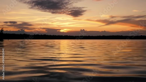 A tranquil golden sunset reflecting over a calm lake with a silhouetted treeline in the distance.