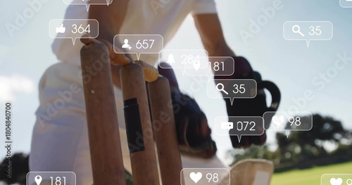 Reaching cricketer in white uniform touching stumps with glove on grassy pitch, social overlay