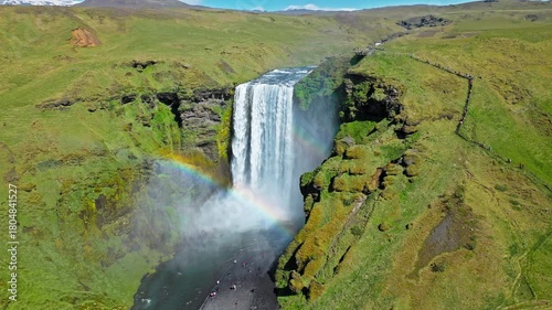 Aerial view of Skogafoss waterfall and surrounding hills. Drone footage showing the river carving through rugged terrain leading toward the tall waterfall.