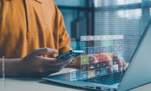 person uses a smartphone and laptop with a holographic digital calendar interface, representing online scheduling, task planning, productivity management, and modern digital workflow technology.