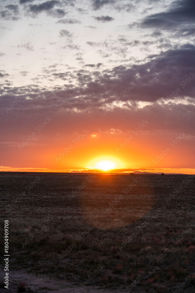 Fototapeta premium The sun sets over a vast field with a colorful sunset