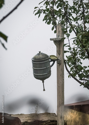 Canvas Print An antique washbasin hangs on a wooden pole in the yard