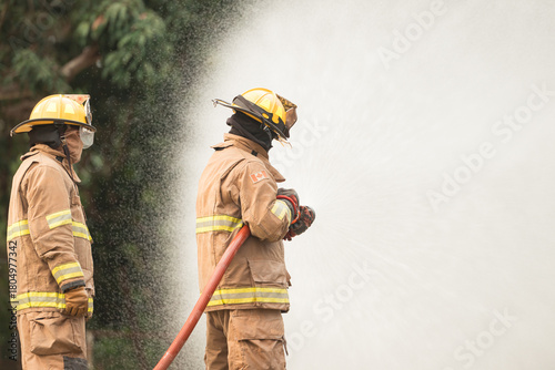 Two firefighters standing in position while directing a powerful water stream at a large blaze