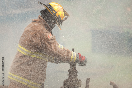 A firefighter in protective gear manually turns off a water valve