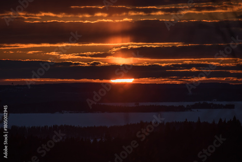 Sunset colours in the clouded sky over forested lake landscape in winter in Finland