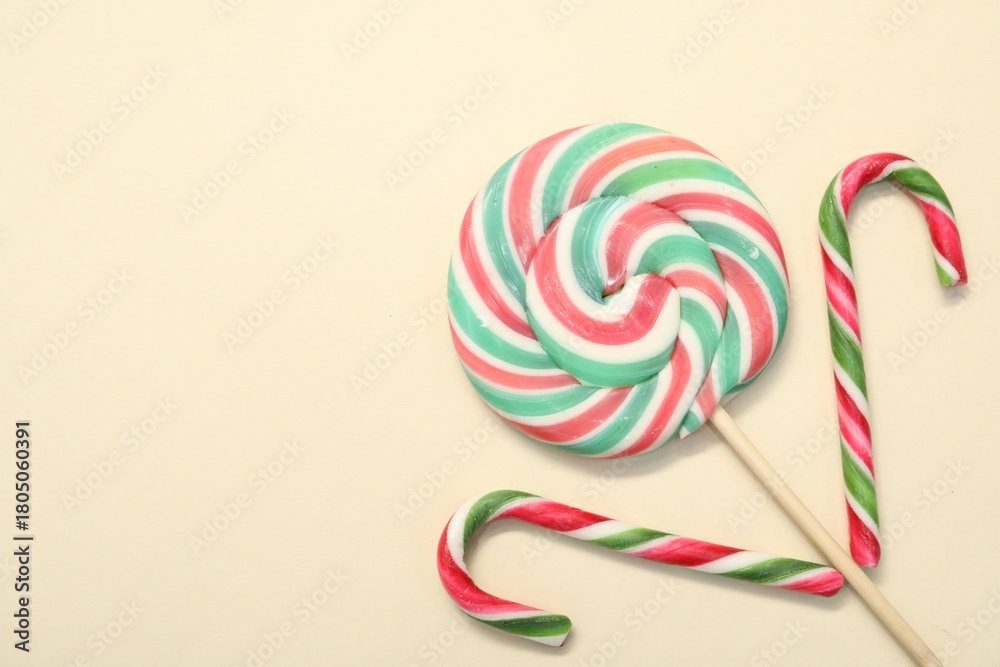 Fototapeta premium Christmas treat. Lollipop and candy canes on beige background, top view. Space for text