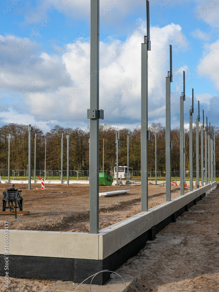 Naklejka premium Steel structural columns installed on concrete foundation at early-stage construction site