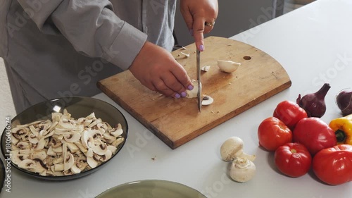 A woman's hands slice champignons on a table with vegetables. Medium shot.