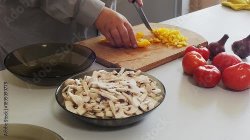 A woman's hands slice yellow peppers on a table with vegetables. Medium shot.