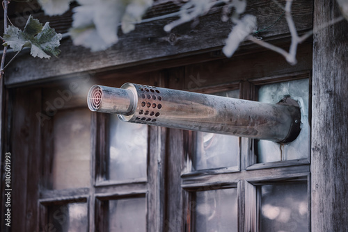 Exhaust pipe protruding from a broken window in a vintage wooden house