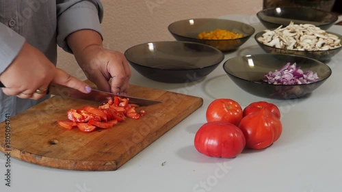 A woman's hands slice red tomatoes on a cutting board on a table. Medium shot.