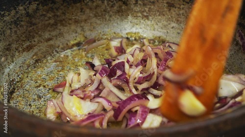 Red onions marinated in soy sauce and spices are fried in a frying pan. Medium shot.