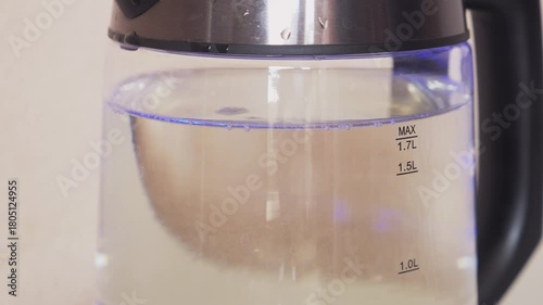 A transparent electric kettle with a blue backlight is bubbling and boiling. Medium shot.