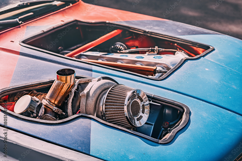 Naklejka premium Close up of a racing car engine, a large turbocharger and air filter protruding from the hood, symbolizing power and speed