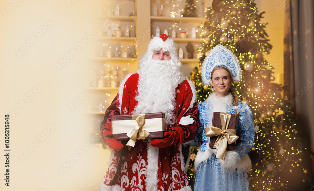 Naklejka premium Ded moroz and snegurochka celebrating holidays with gifts in front of festive christmas tree, copy space