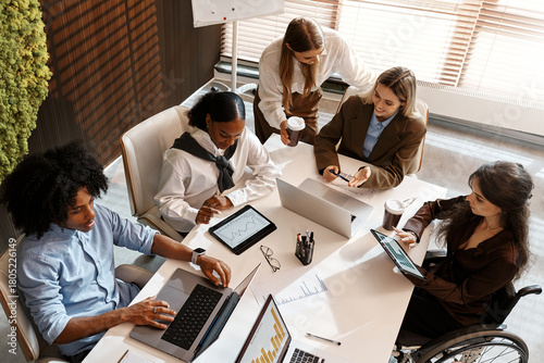 Diverse business team analyzing charts during office meeting from top view