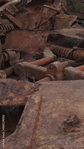 rusted tank hull and wheel parts scattered across scrapyard; close-up of corroded machinery, flaking patina,
