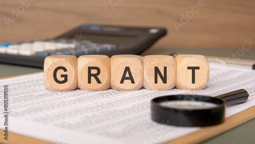 Wooden cubes spelling GRANT on financial papers, symbolizing non-repayable funding.