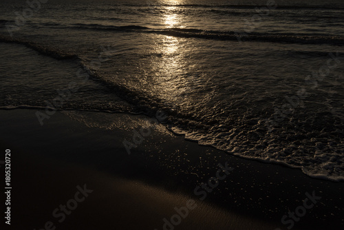 Olas oscuras rompiendo en la orilla con el reflejo dorado del sol poniente o naciente, capturado en la costa de Córdoba, Colombia. Dramatismo, brillo y tranquilidad en el mar.