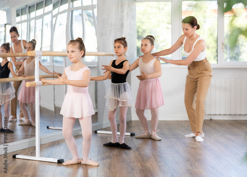 Naklejka premium Girls children students of ballet school near ballet bare performs grand demi plie under guidance of experienced female mentor. Training program for members of ballet troupe of theater