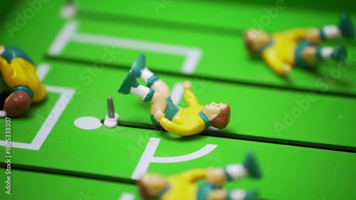 Dynamic shot moving from midfield to an empty foosball goal. Players lying on the field after a dramatic play. Competition, tension, tabletop soccer game scene.
