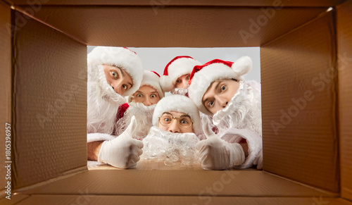 Fotografie Group portrait shows happy Santas peeking into gift box, celebrating New Year or Christmas, infusing holiday fun, transforming the space into a festive hub where group curiosity and joy reign supreme
