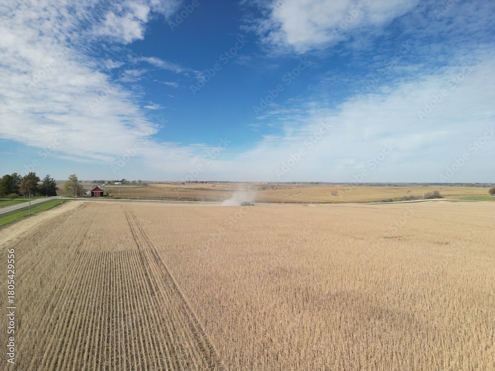 Obraz premium High above the rural Midwest landscapes on a crisp fall day harvest is blowing out lots of dust as the machines make its way down the field bringing in grain. 