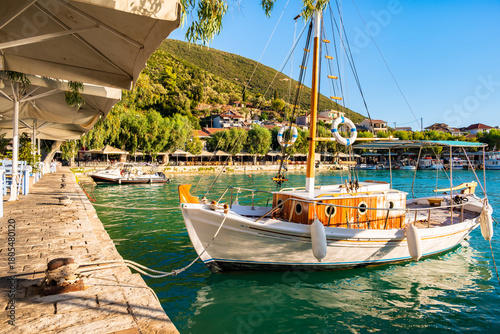Greek taverna tables and traditional wooden fishing boat anchored in Vassilik...