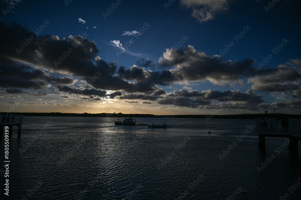 Obraz premium fishing boat on calm water, tropical beach and colorful sunset sky, serene landscape coastal view with wooden pier, cloudy evening, travel and nature tranquility horizon with green vegetation