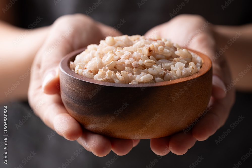 Fototapeta premium Cooked Thai brown rice in a wooden bowl holding by hand, Healthy eating