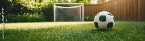 Classic black and white soccer ball rests on lush green grass near goalpost in backyard, evoking calm and inviting atmosphere