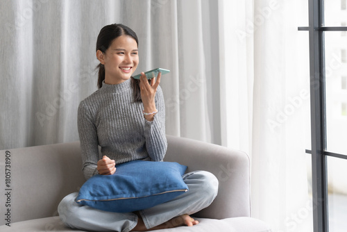Asian woman using voice assistant on smartphone at home conversation with online assistant Voice chat bot conversational AI Modern Technologies.
