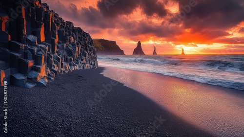 basalt column cliff on black pebble beach at fiery sunset with distant sea stacks, crashing waves and reflective wet sand, dramatic awe-inspiring atmosphere