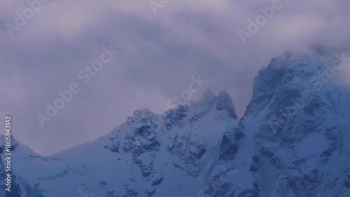 A drone shot of a majestic mountain range in the North Caucasus region of Russia, blanketed in snow under a dramatic, cloudy sky.
