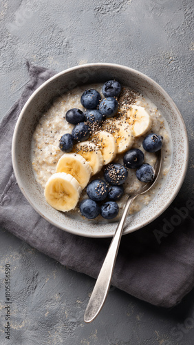 
Breakfast oatmeal porridge with banana, blueberries, chia seeds on grey concrete background. Table top view of healthy food for weight loss, clean eating, vegan and vegetarian diet