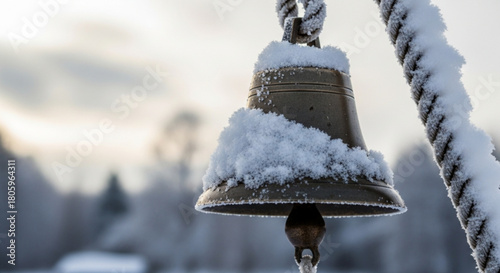 A closeup shot captures a snowcovered bell, suspended by a rope, against a blurred winter landscape, evoking the serene beauty of the season