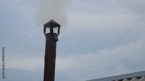 Smoke from a small chimney against a cloudy sky. A small rural bathhouse is being heated