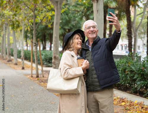 Quadro su tela Happy senior couple enjoying autumn walk and taking a selfie with copy space