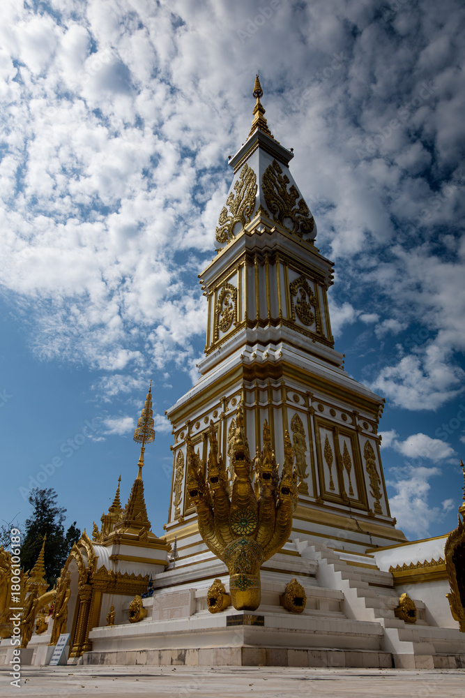 Fototapeta premium Phra That Ming Mueang Maru Nakhon stupa with ornate gold carvings, Buddha statues, and naga serpents. Sacred Thai temple showcasing intricate architecture, cultural heritage, and spiritual atmosphere