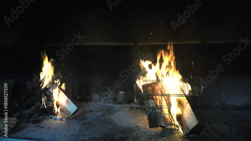 Two bonfires burn wood in a space designated for barbecues; the place is dark because it's nighttime for dinner.