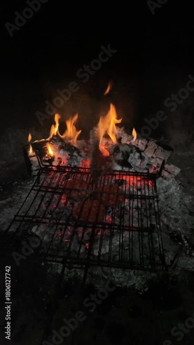 Three hamburgers are being cooked on grills over the embers of a bonfire, a barbecue night