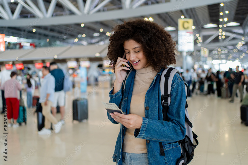 Fototapeta premium Latino woman talking on phone while walking through airport terminal. 