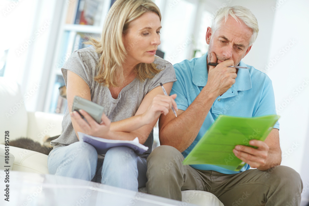 Obraz premium Mature couple, document and calculator in home for finance, budget or tax compliance for income. Thinking, man and woman with discussion, paperwork or review of bills or debt for investing in house